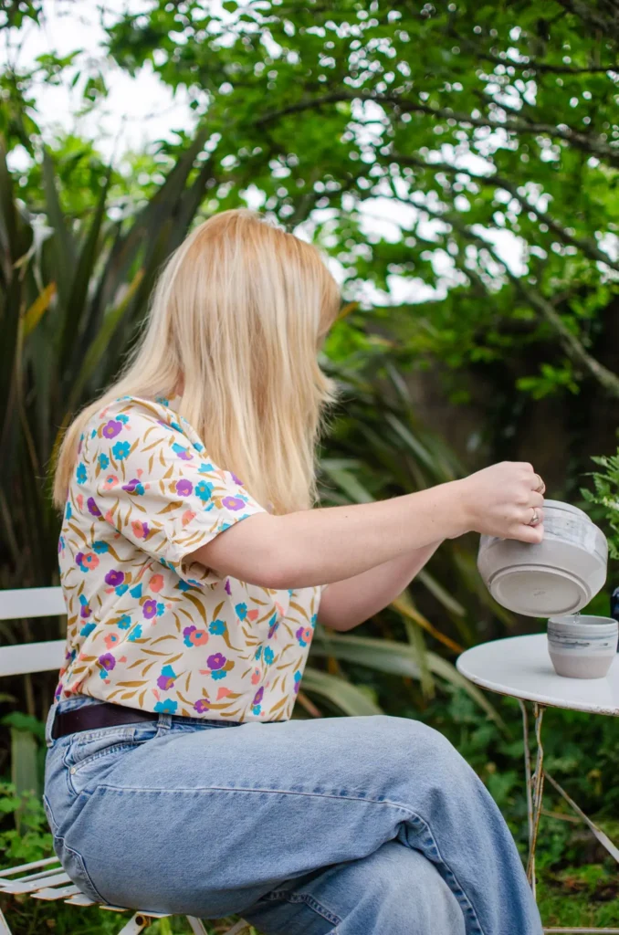 Kiara se sert une tasse de thé. elle porte son chemisier Dalhia et un jean